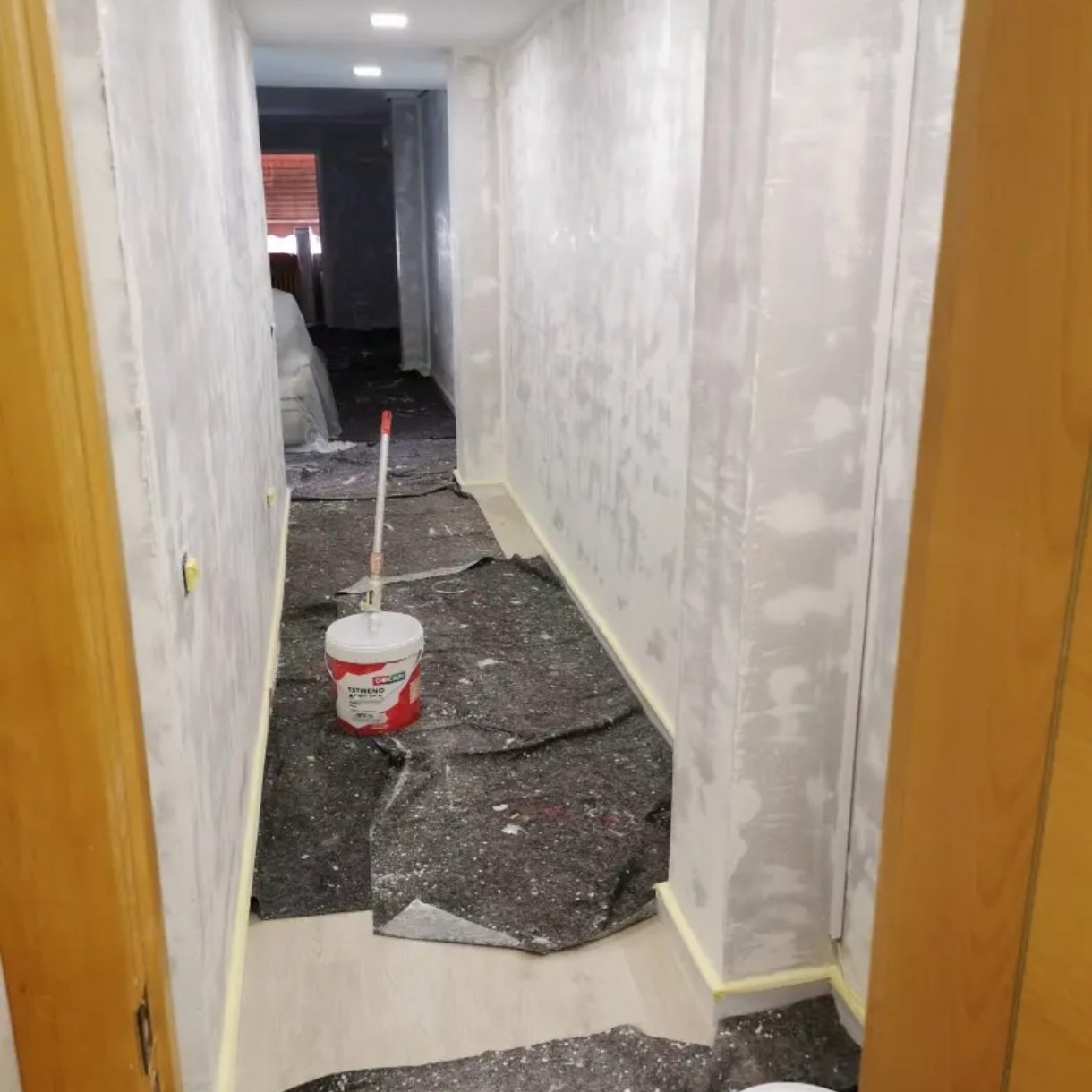 Pasillo en construcción con paredes sin terminar y cubiertas en el suelo.